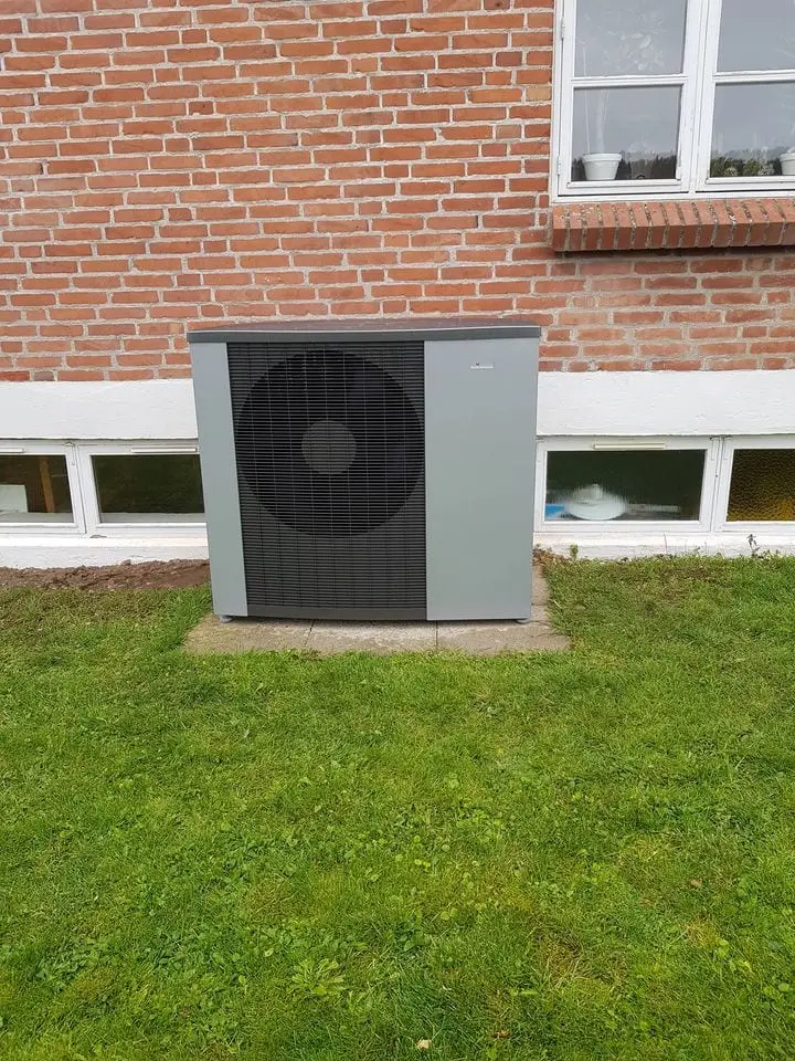 Udedel til luft/vand-varmepumpe monteret op ad en rød murstensvæg